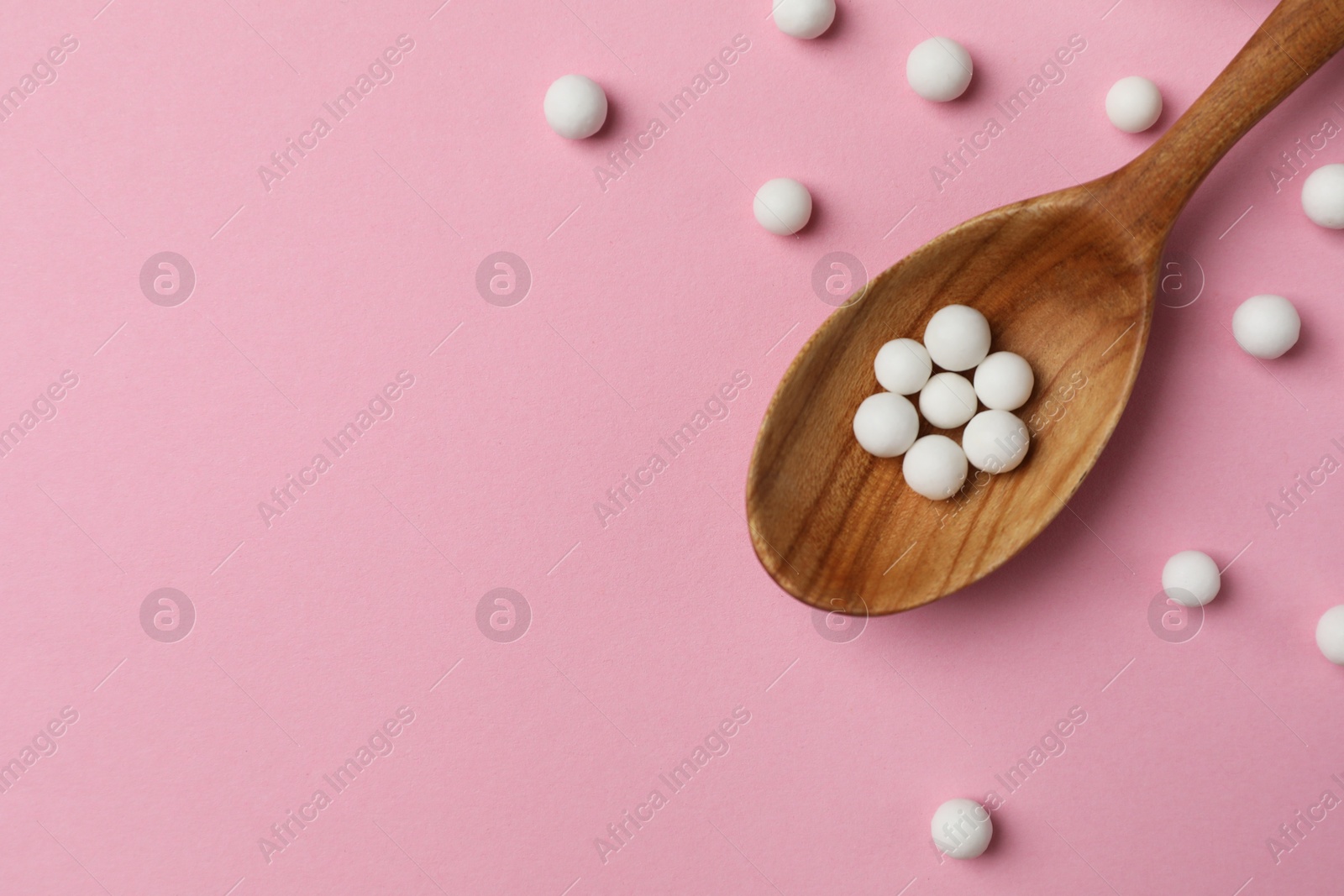 Photo of Homeopathic remedy. Wooden spoon and pills on pink background, top view. Space for text