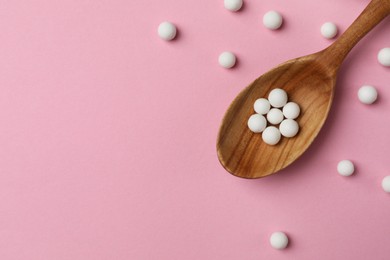 Homeopathic remedy. Wooden spoon and pills on pink background, top view. Space for text