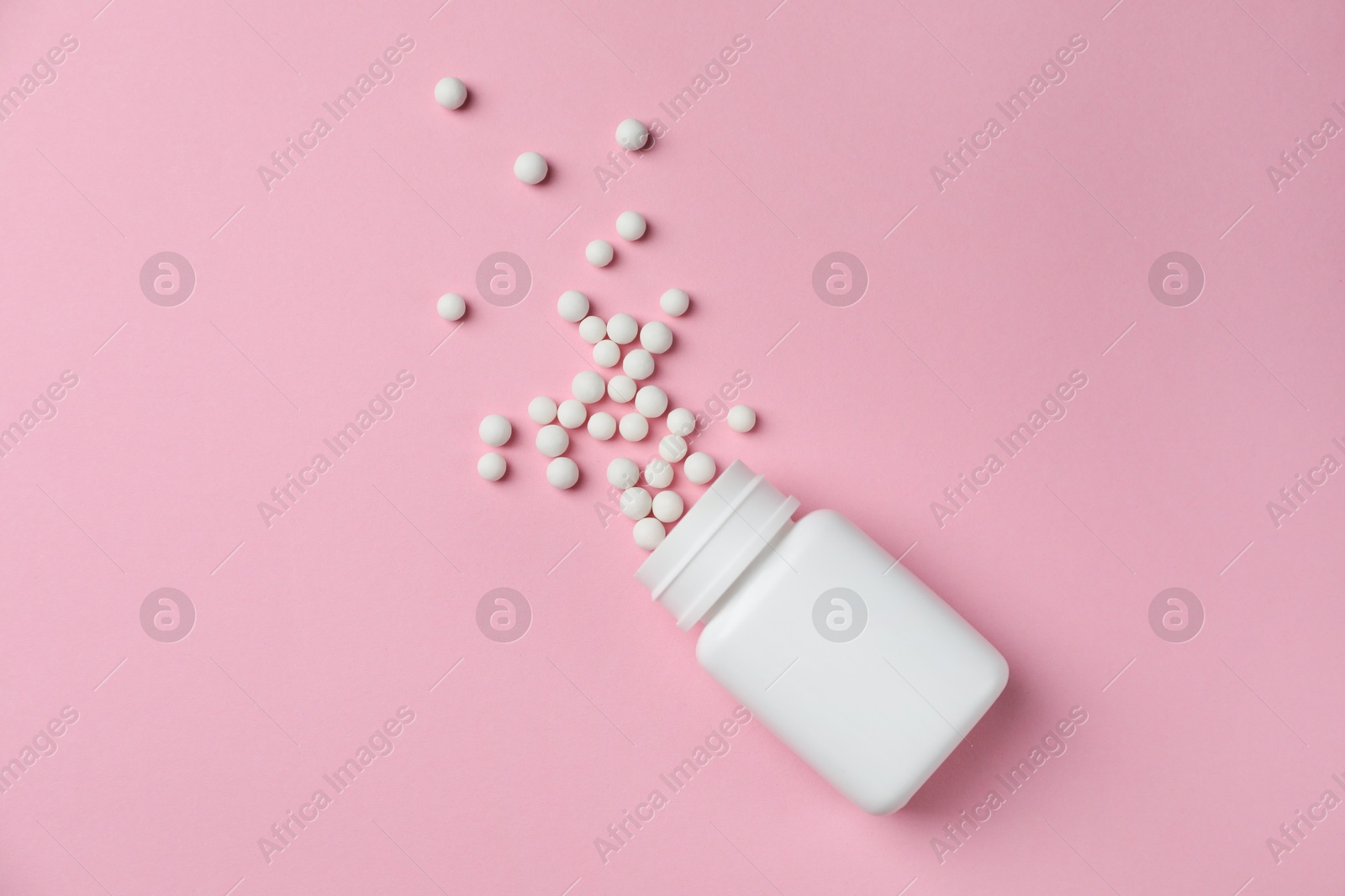 Photo of Homeopathic remedy. Overturned plastic bottle and pills on pink background, top view