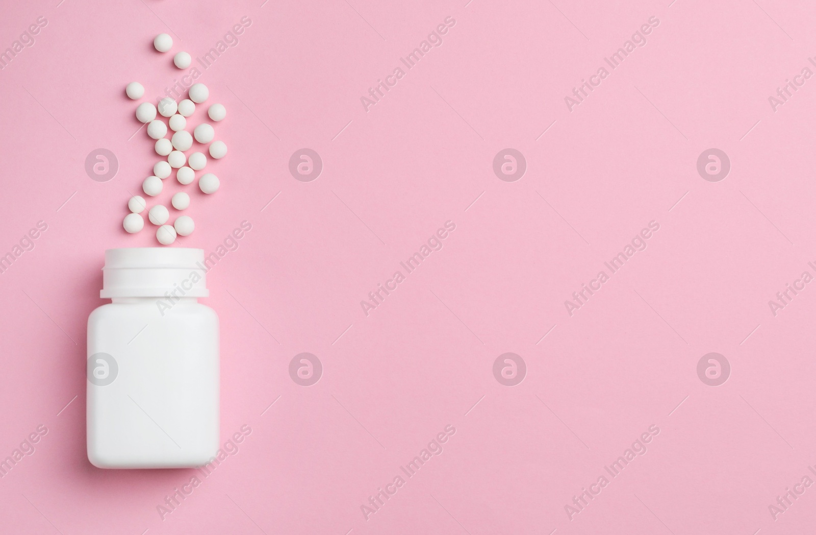 Photo of Homeopathic remedy. Overturned plastic bottle and pills on pink background, top view. Space for text