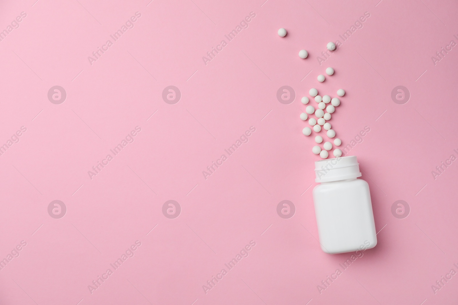 Photo of Homeopathic remedy. Overturned plastic bottle and pills on pink background, top view. Space for text