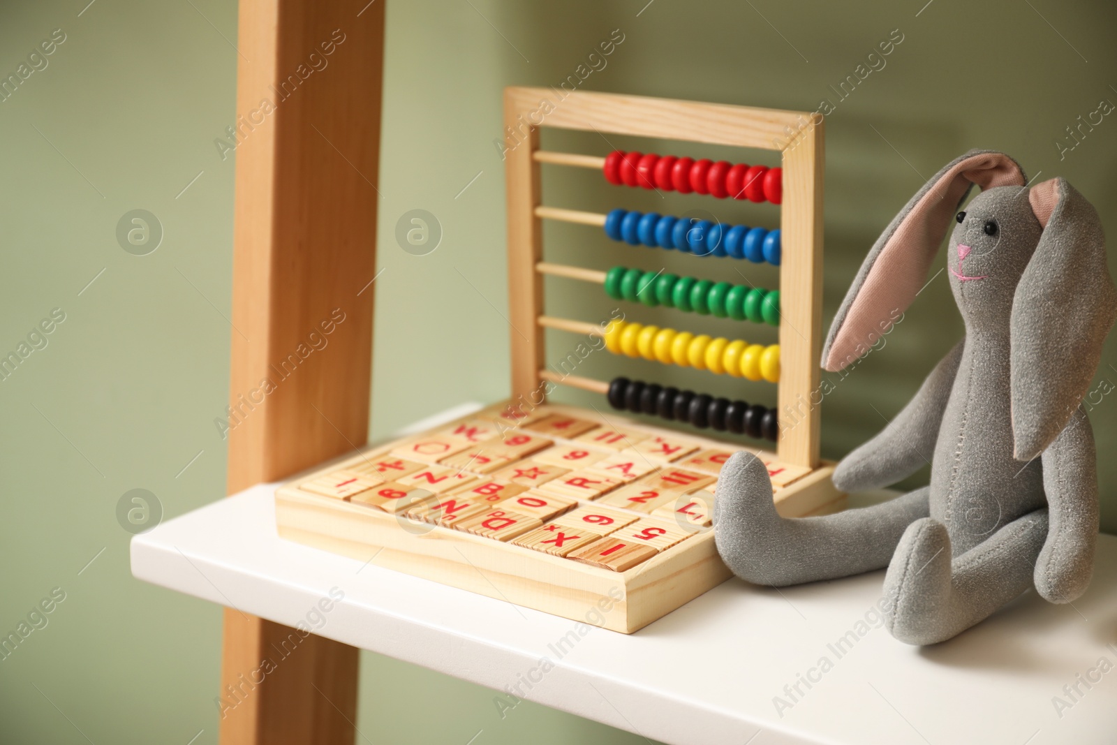 Photo of Bunny toy, wooden cubes and abacus near olive wall