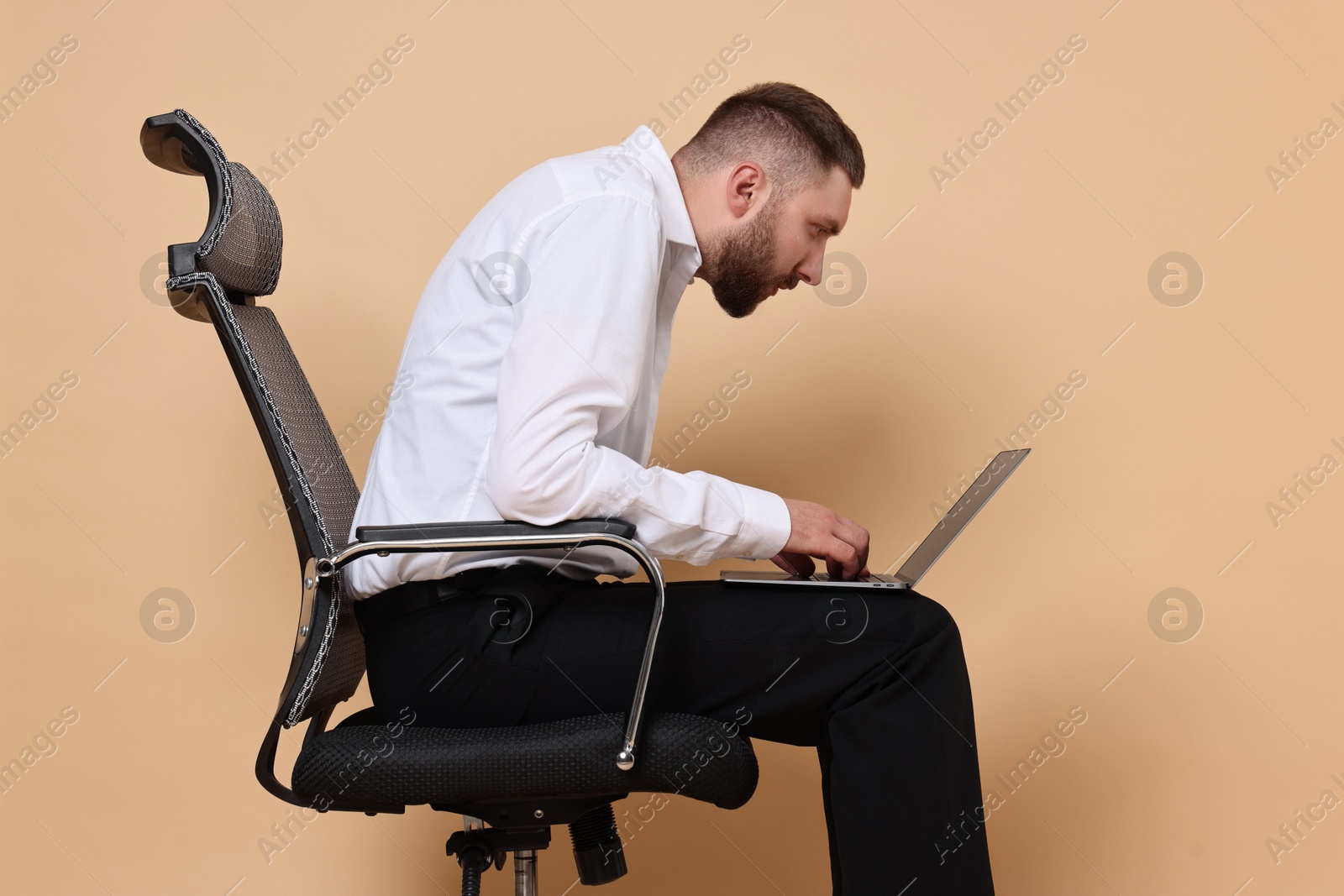 Photo of Man with poor posture sitting on chair and using laptop against pale orange background