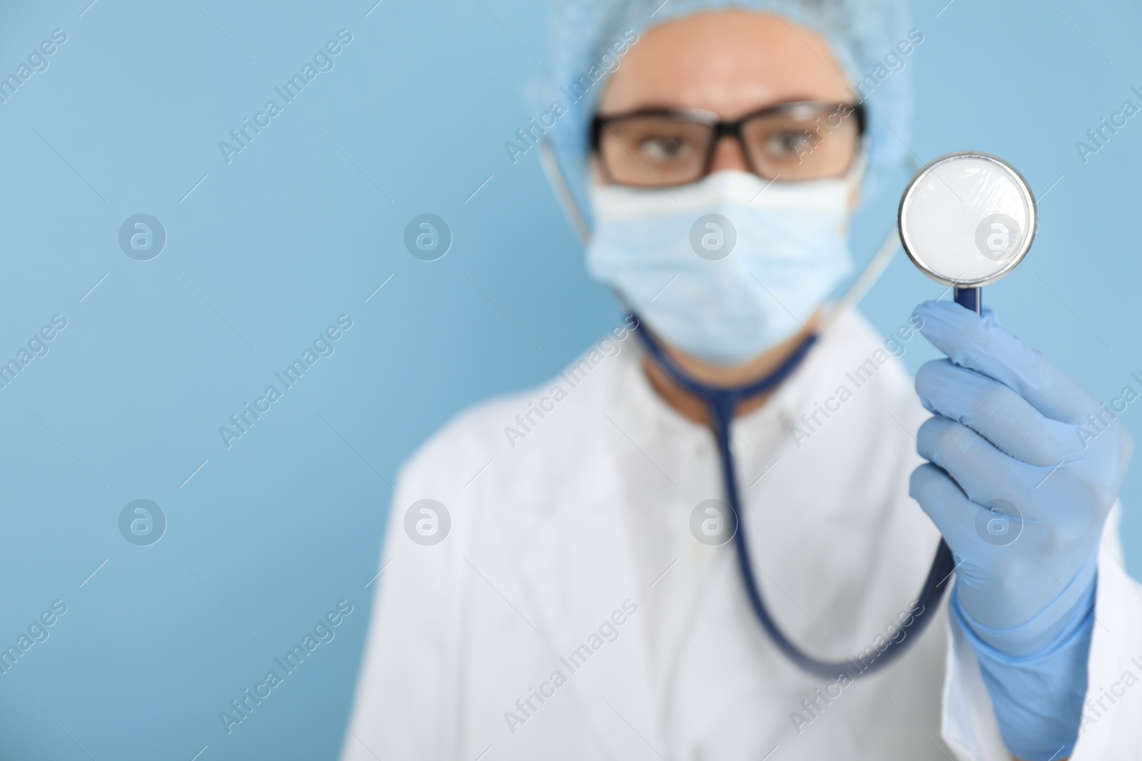 Photo of Doctor holding stethoscope on light blue background, selective focus