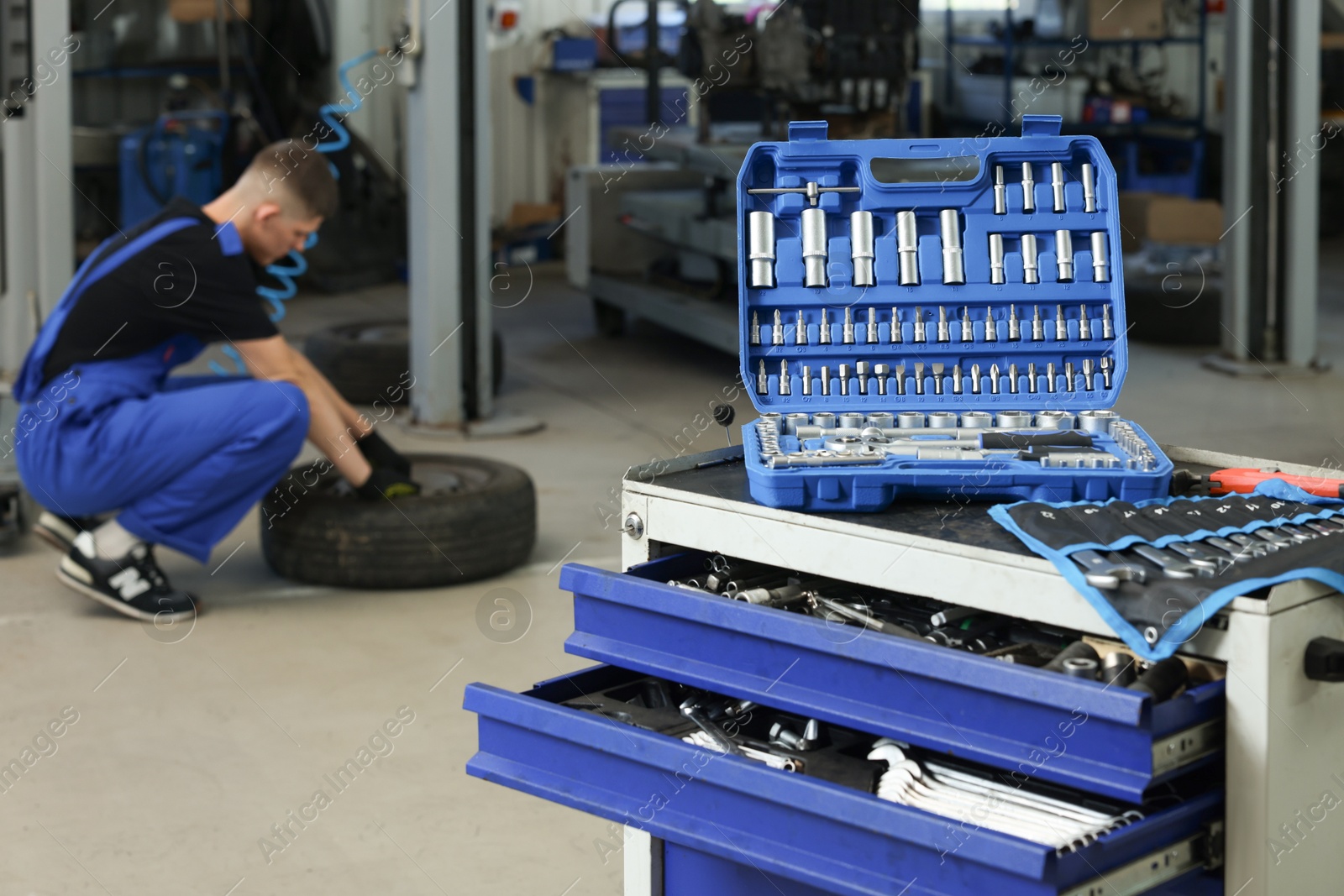 Photo of Auto mechanic with tire, focus on different tools at automobile repair shop