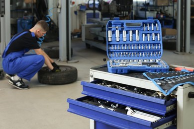 Auto mechanic with tire, focus on different tools at automobile repair shop