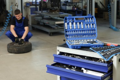 Photo of Auto mechanic with tire, focus on different tools at automobile repair shop