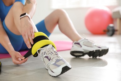 Photo of Beautiful woman putting on ankle weights indoors, closeup