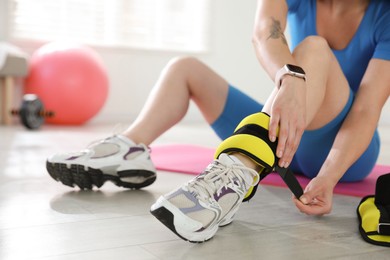 Photo of Beautiful woman putting on ankle weights indoors, closeup