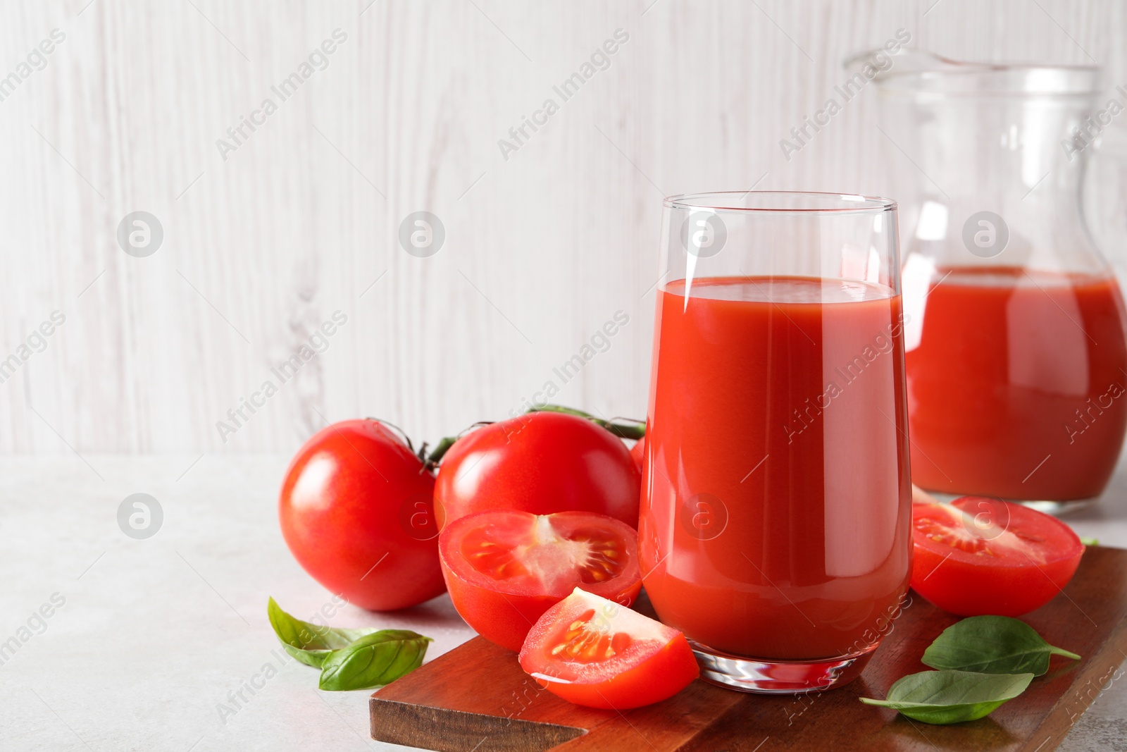 Photo of Tasty tomato juice in glass, basil leaves and fresh vegetables on light grey table. Space for text