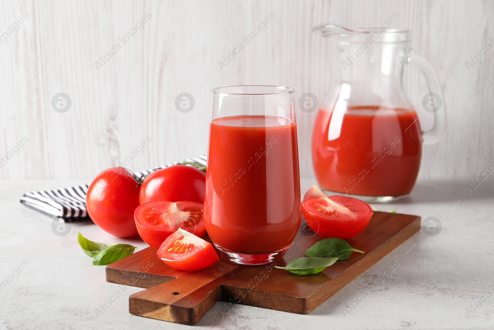 Photo of Tasty tomato juice in glass, basil leaves and fresh vegetables on light grey table