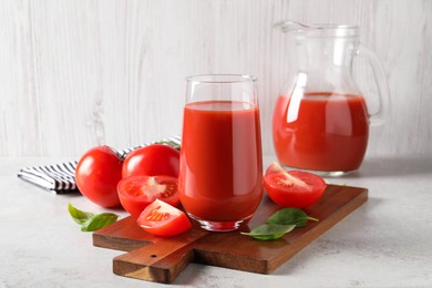 Tasty tomato juice in glass, basil leaves and fresh vegetables on light grey table