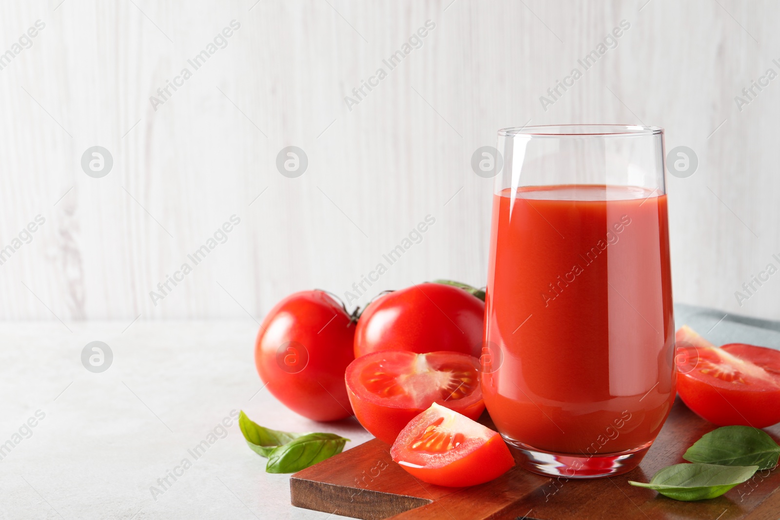 Photo of Tasty tomato juice in glass, basil leaves and fresh vegetables on light grey table. Space for text