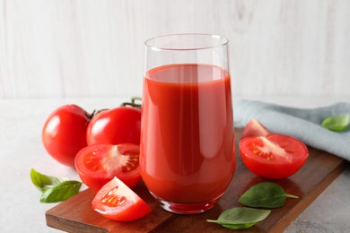 Tasty tomato juice in glass, basil leaves and fresh vegetables on light grey table