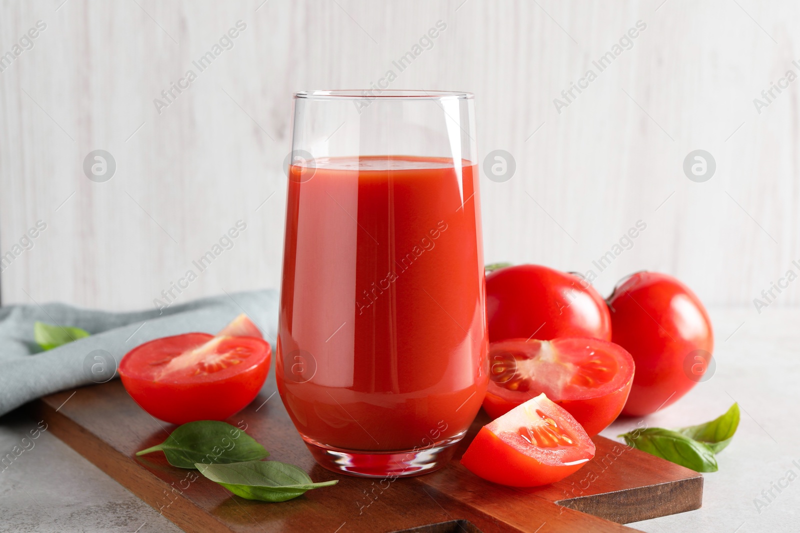 Photo of Tasty tomato juice in glass, basil leaves and fresh vegetables on light grey table