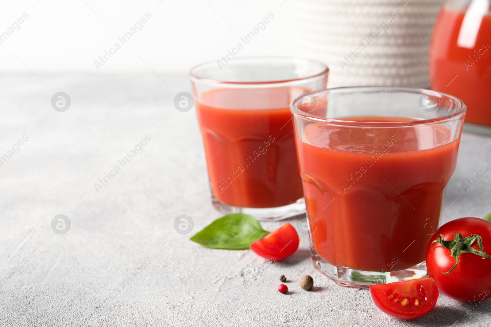 Photo of Tasty tomato juice in glasses, basil, peppercorns and fresh vegetables on light grey table, space for text