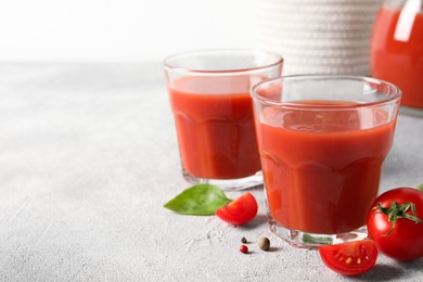 Tasty tomato juice in glasses, basil, peppercorns and fresh vegetables on light grey table, space for text