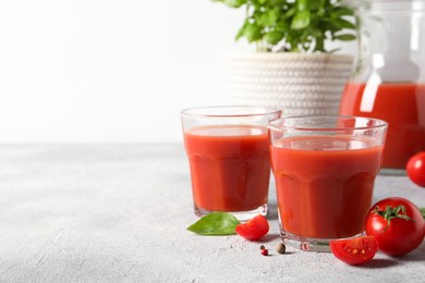 Photo of Tasty tomato juice in glasses, basil, peppercorns and fresh vegetables on light grey table, space for text