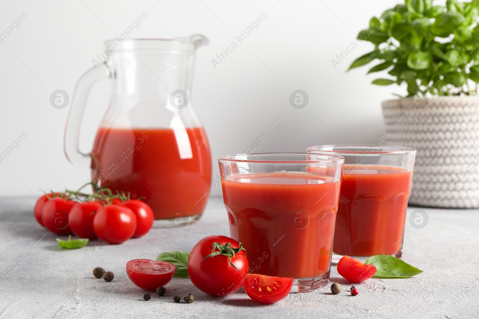 Photo of Tasty tomato juice in glasses, jug, basil, peppercorns and fresh vegetables on light grey table