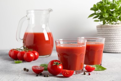 Tasty tomato juice in glasses, jug, basil, peppercorns and fresh vegetables on light grey table