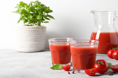 Photo of Tasty tomato juice in glasses, basil, peppercorns and fresh vegetables on light grey table