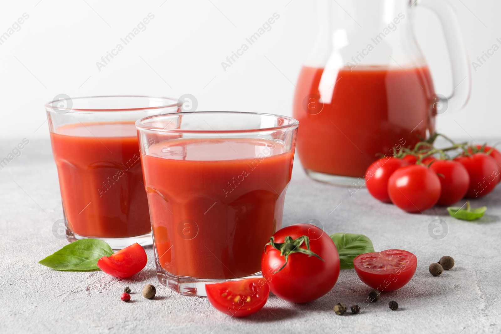 Photo of Tasty tomato juice in glasses, basil, peppercorns and fresh vegetables on light grey table