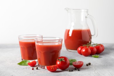 Photo of Tasty tomato juice in glasses, jug, basil, peppercorns and fresh vegetables on light grey table