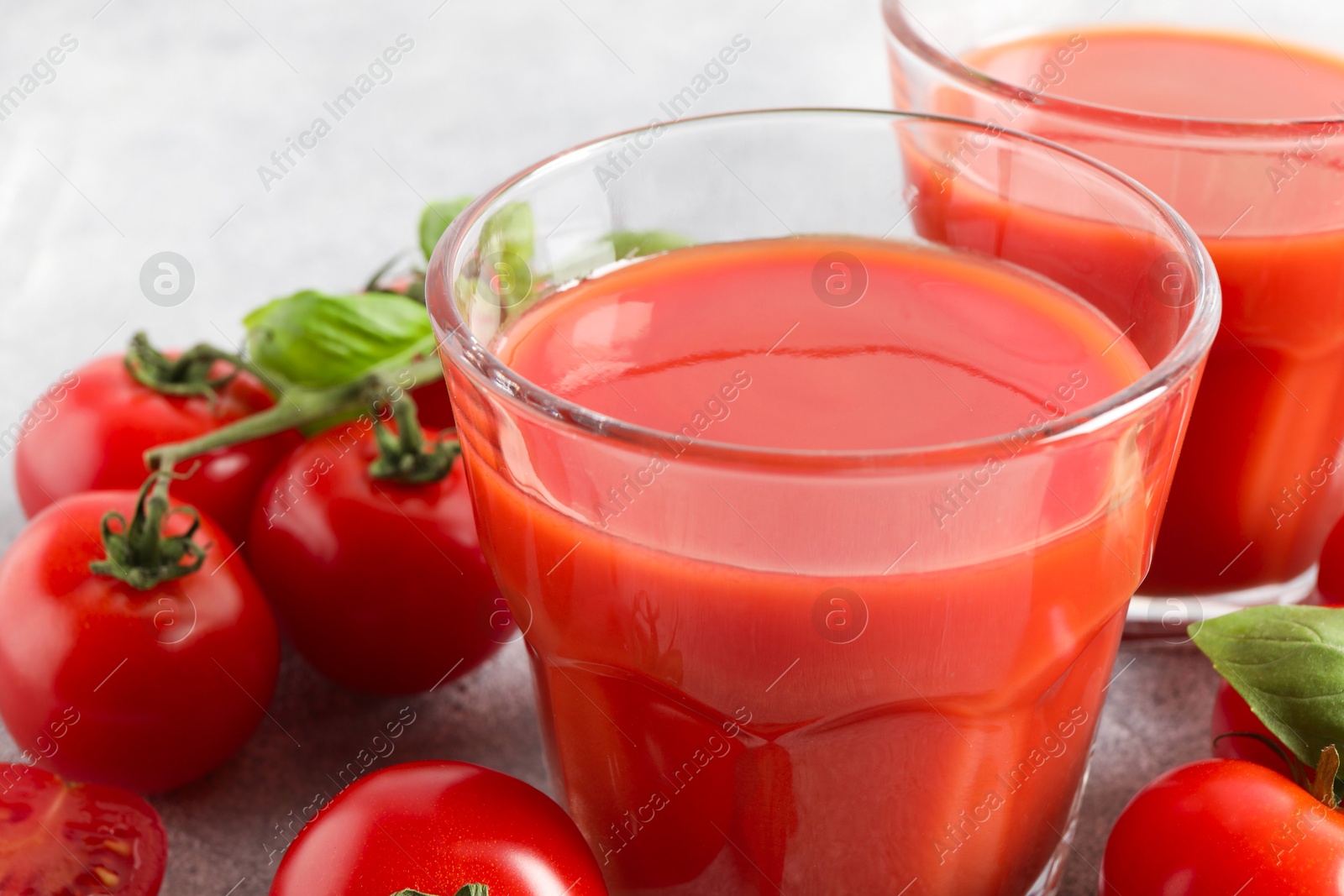 Photo of Tasty tomato juice in glasses, basil and fresh vegetables on table, closeup