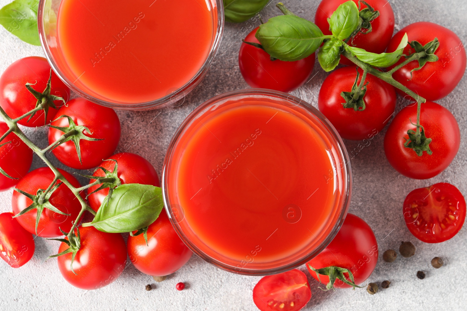 Photo of Tasty tomato juice in glasses, basil leaves, fresh vegetables and peppercorns on light grey table, flat lay