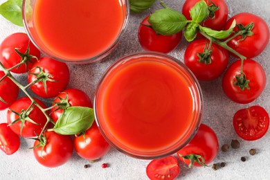 Photo of Tasty tomato juice in glasses, basil leaves, fresh vegetables and peppercorns on light grey table, flat lay