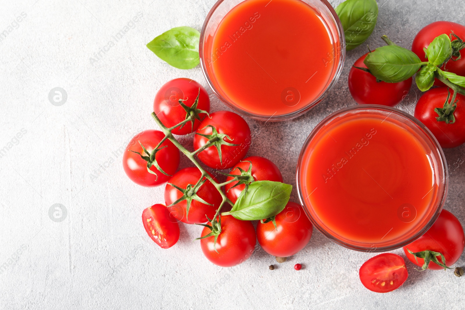 Photo of Tasty tomato juice in glasses, basil leaves, fresh vegetables and peppercorns on light grey table, flat lay. Space for text