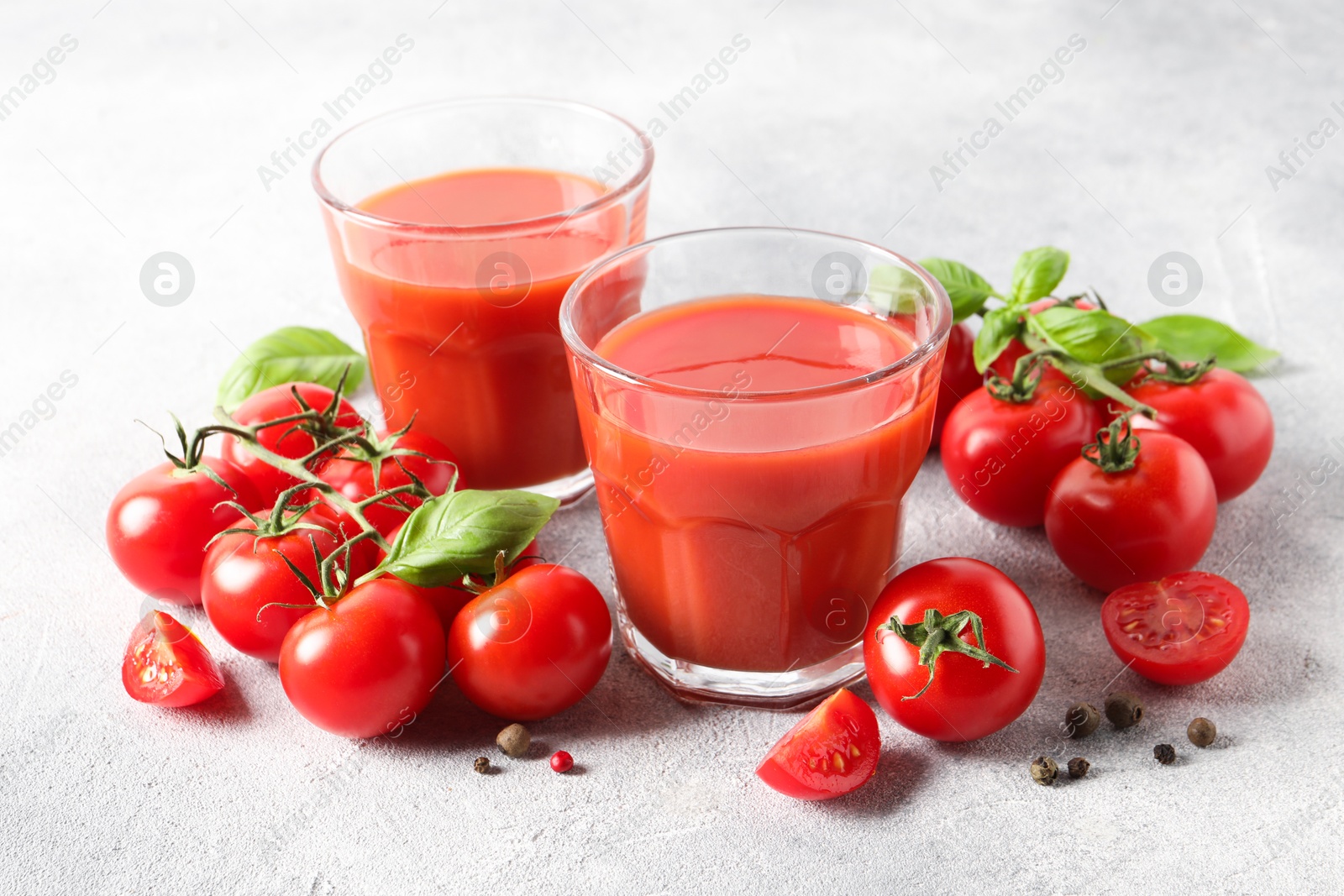 Photo of Tasty tomato juice in glasses, basil leaves, fresh vegetables and peppercorns on light grey table