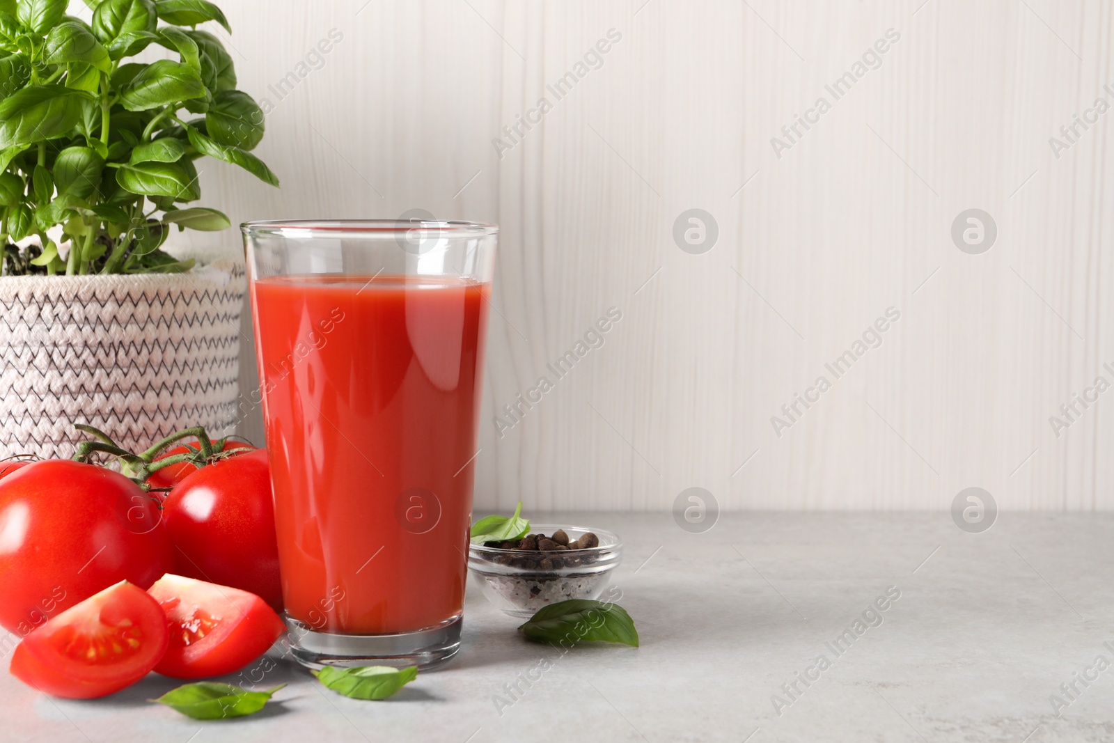 Photo of Tasty tomato juice in glass, basil leaves, peppercorns and fresh vegetables on light grey table, space for text