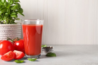 Tasty tomato juice in glass, basil leaves, peppercorns and fresh vegetables on light grey table, space for text