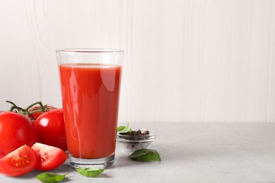 Photo of Tasty tomato juice in glass, basil leaves, peppercorns and fresh vegetables on light grey table, space for text