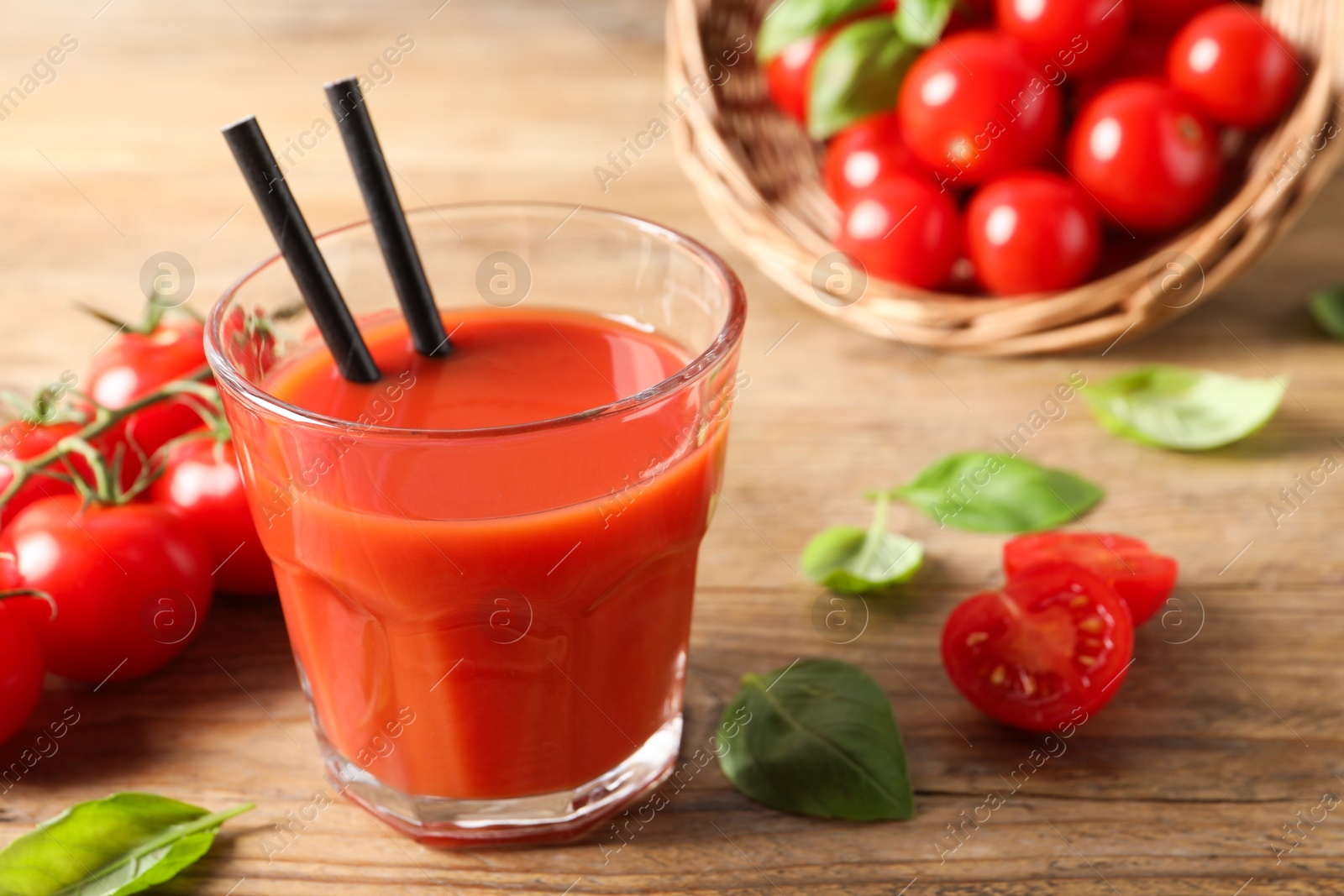 Photo of Tasty tomato juice in glass, basil leaves and fresh vegetables on wooden table