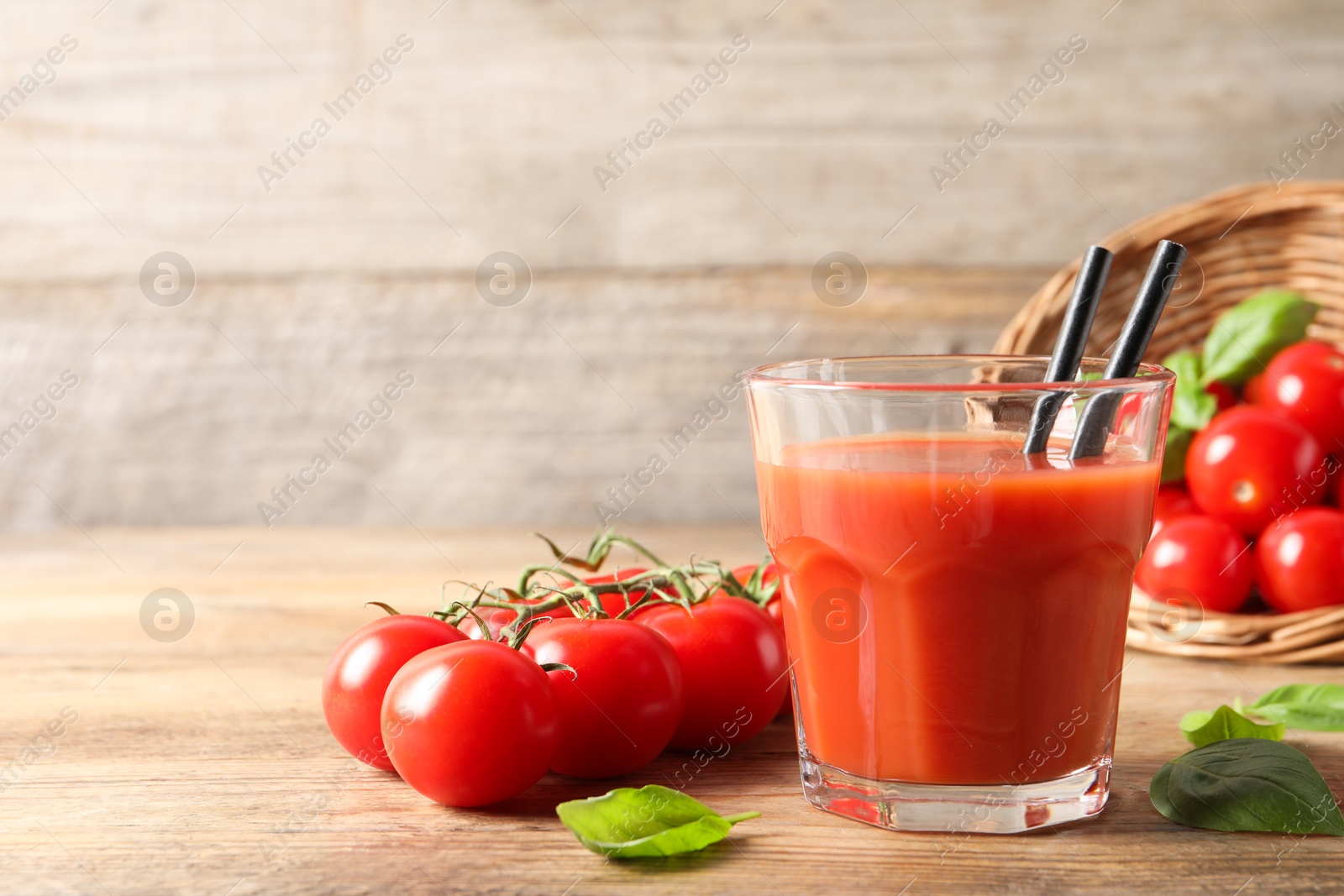 Photo of Tasty tomato juice in glass, basil leaves and fresh vegetables on wooden table. Space for text