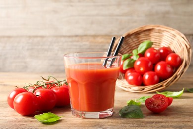 Photo of Tasty tomato juice in glass, basil leaves and fresh vegetables on wooden table