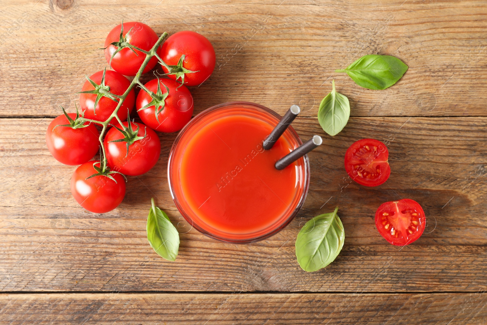 Photo of Tasty tomato juice in glass, basil leaves and fresh vegetables on wooden table, flat lay