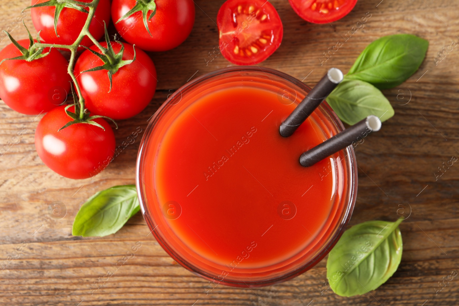 Photo of Tasty tomato juice in glass, basil leaves and fresh vegetables on wooden table, flat lay