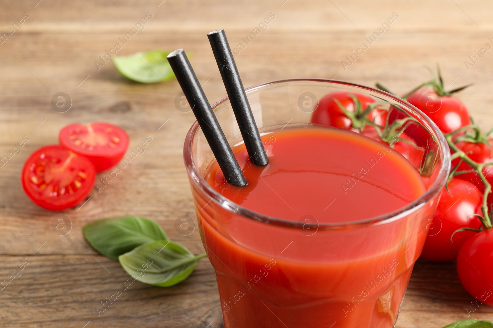 Photo of Tasty tomato juice in glass, basil leaves and fresh vegetables on wooden table, closeup