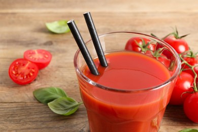 Photo of Tasty tomato juice in glass, basil leaves and fresh vegetables on wooden table, closeup