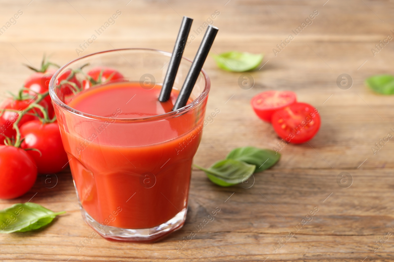 Photo of Tasty tomato juice in glass, basil leaves and fresh vegetables on wooden table. Space for text