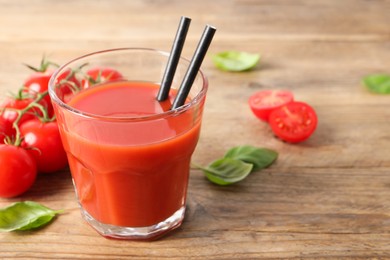 Photo of Tasty tomato juice in glass, basil leaves and fresh vegetables on wooden table. Space for text