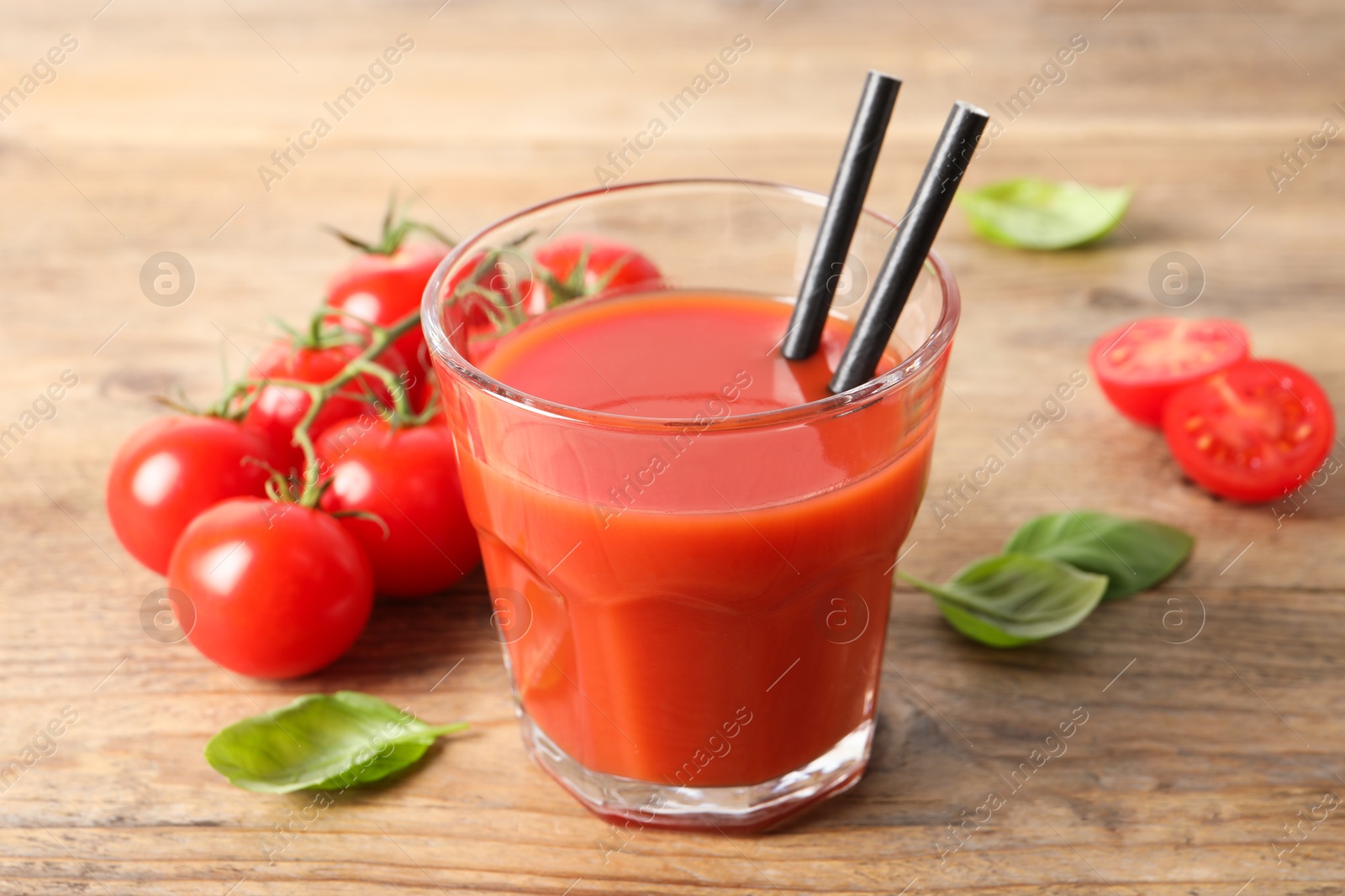 Photo of Tasty tomato juice in glass, basil leaves and fresh vegetables on wooden table