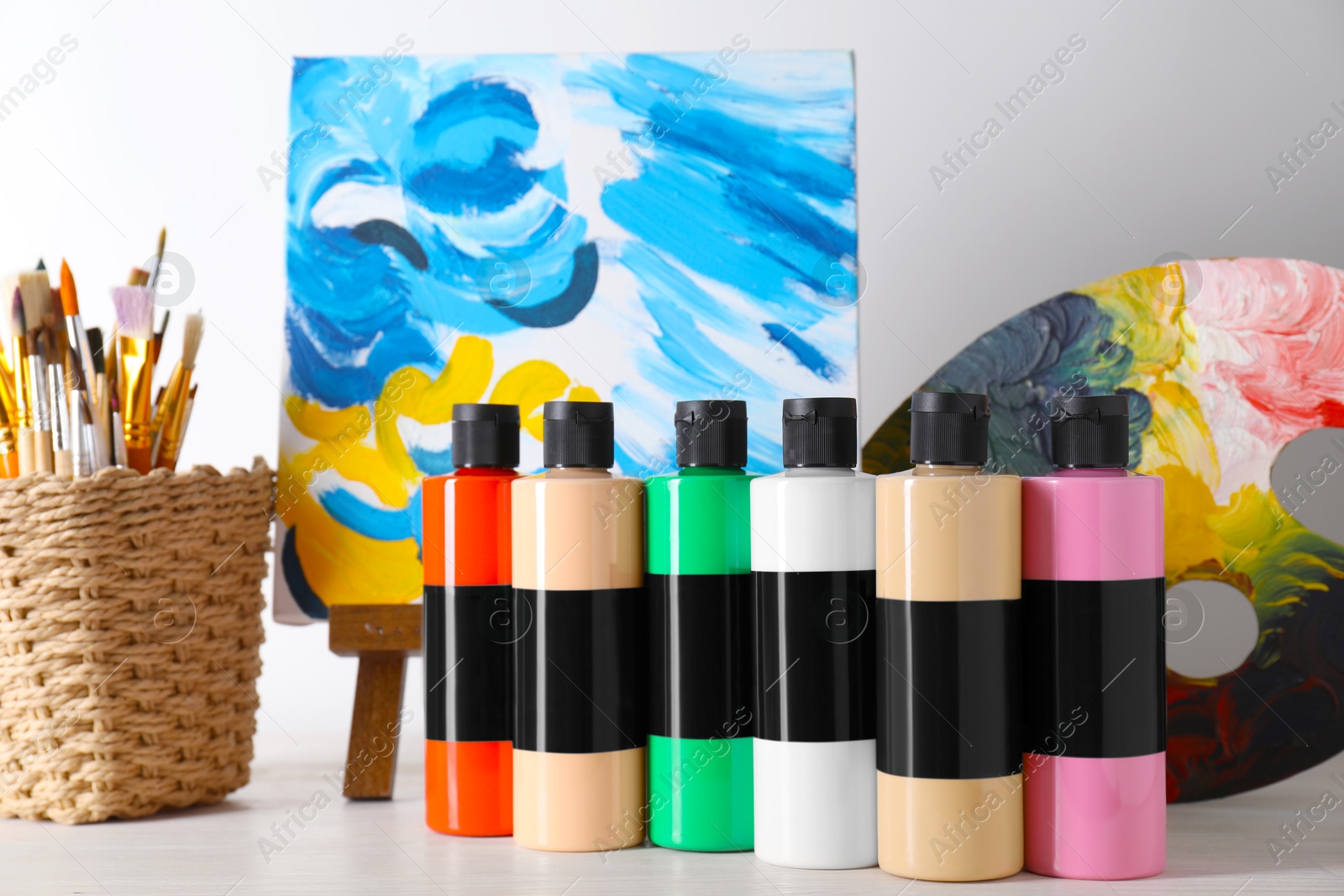 Photo of Acrylic paints of different colors, small easel with abstract picture, palette and brushes on wooden table