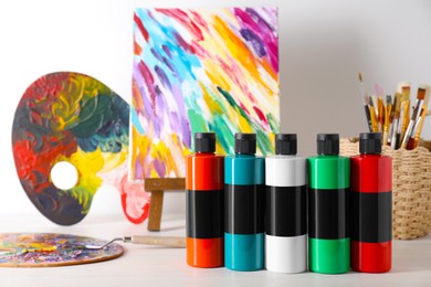 Acrylic paints of different colors, palettes, knife, small easel and brushes on wooden table