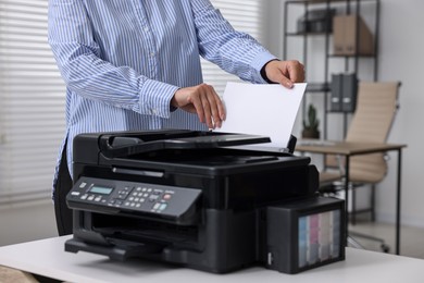 Woman using modern printer at workplace indoors, closeup