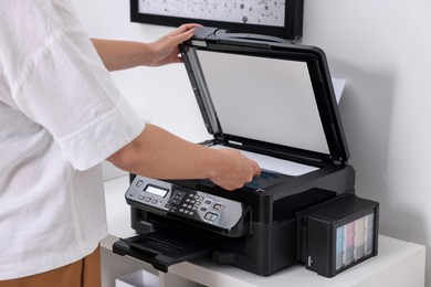 Photo of Woman using modern printer at workplace indoors, closeup