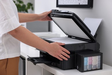 Photo of Woman using modern printer at workplace indoors, closeup